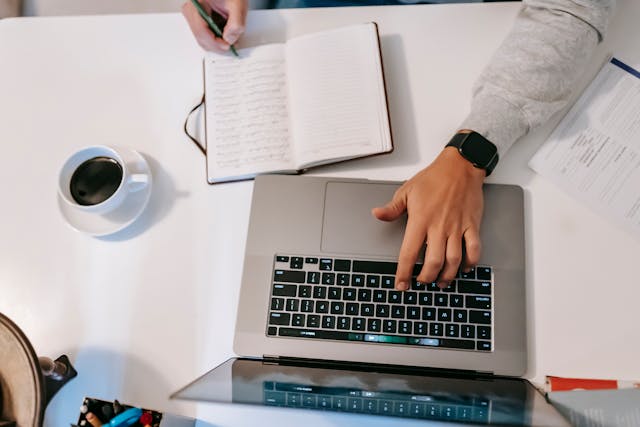 man writing an assignment with laptop open