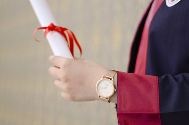 a person wearing an analogue watch and holding a graduation diploma