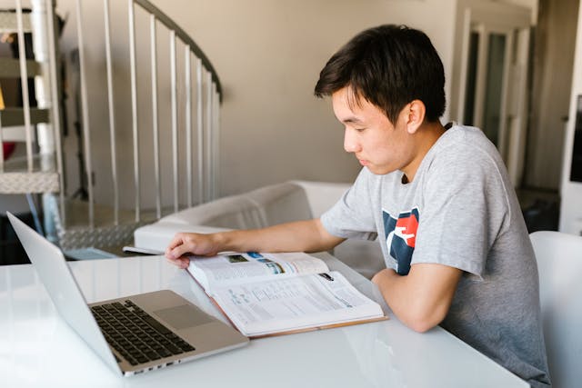 Student taking notes while attending a distance learning class on laptop