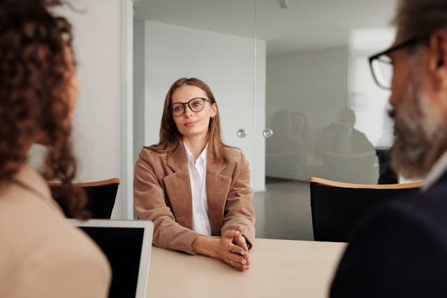 Woman in brown blazer seated beside table for a job interview