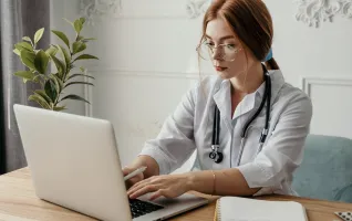 woman doctor wearing white coat and stethoscope typing on laptop