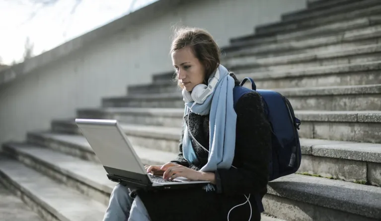 Woman sitting on concrete stairs using her laptop for distance learning studies