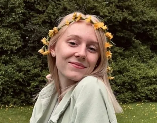 Studentin aus dem Fernstudium Soziale Arbeit mit Blumenkranz im Haar steht lächelnd auf einer Wiese 